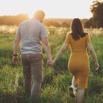 A couple holding hands and walking in a sunny meadow during sunset, capturing a romantic moment.