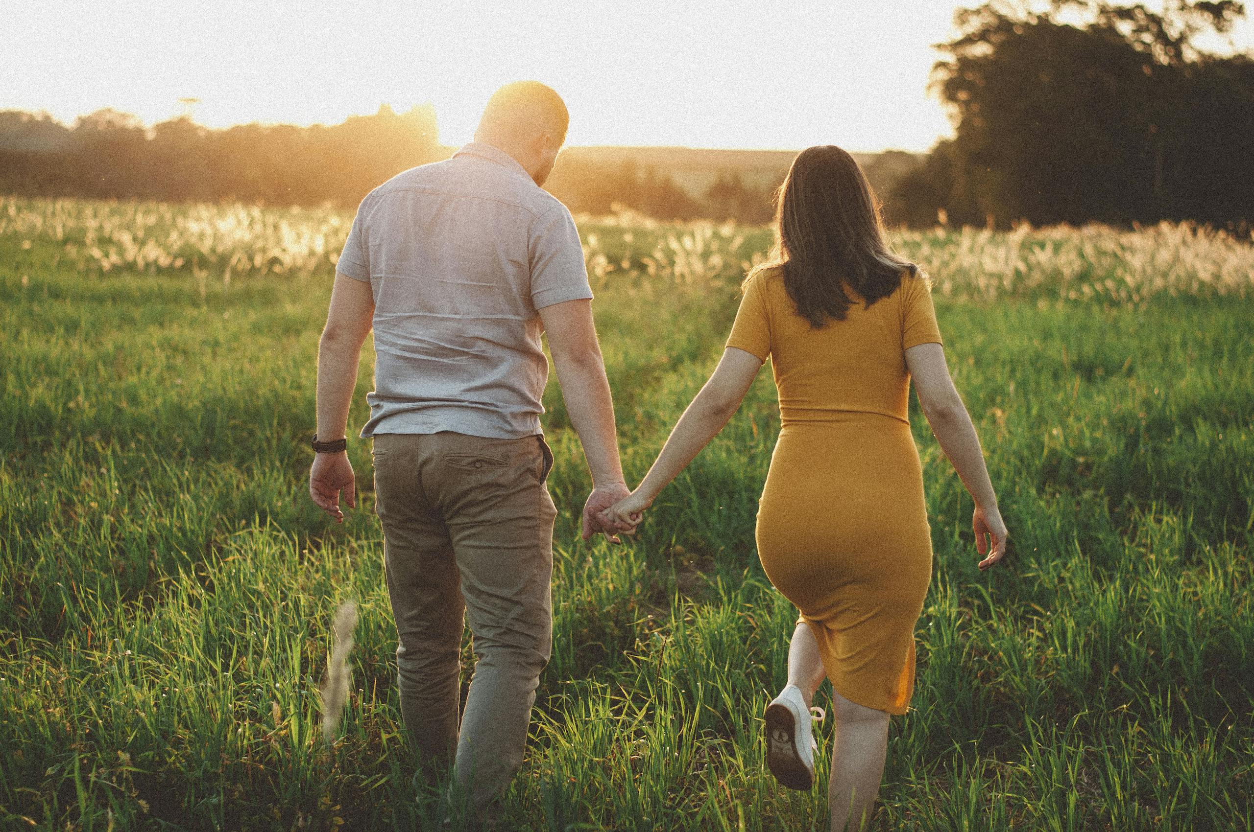 A couple holding hands and walking in a sunny meadow during sunset, capturing a romantic moment.