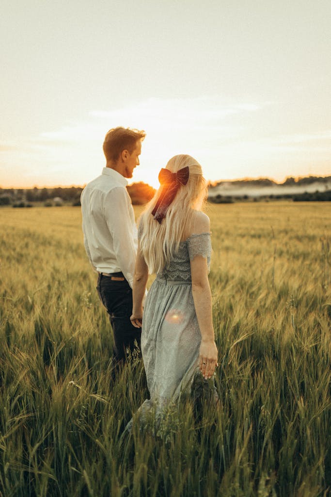 A couple walking hand in hand through a grassy field during a picturesque sunset, showcasing their love.