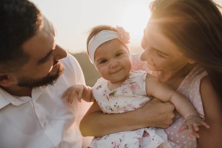 A joyful family scene with parents holding their smiling baby at sunset.