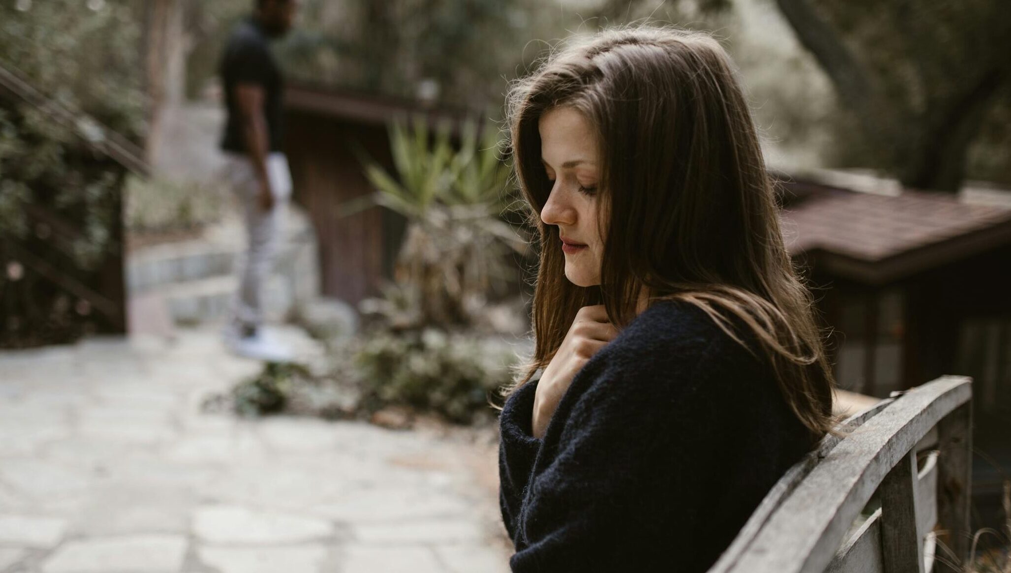 A woman sitting alone on a bench with a distant person, evoking a contemplative mood.