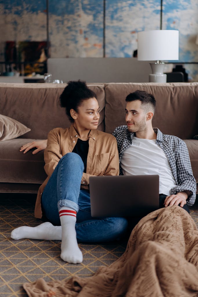 Couple sitting on floor with laptop, sharing a warm and cozy moment.