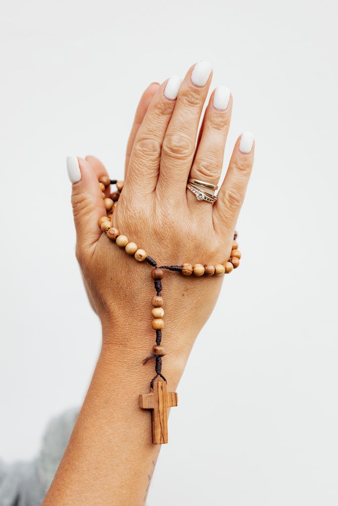 Detailed close-up of hands in prayer holding a wooden rosary with a cross.