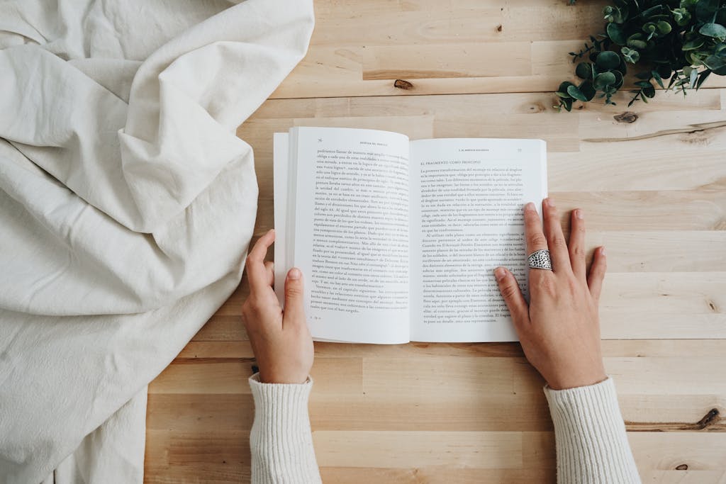 Top view of a person reading a book on a wooden table with a cozy setup, ideal for leisure and learning concepts.