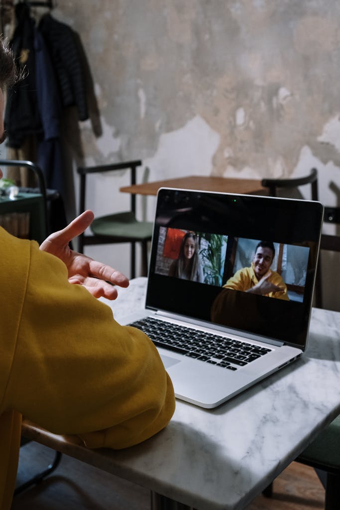 Person in a yellow sweater hosting a video call on a laptop indoors.