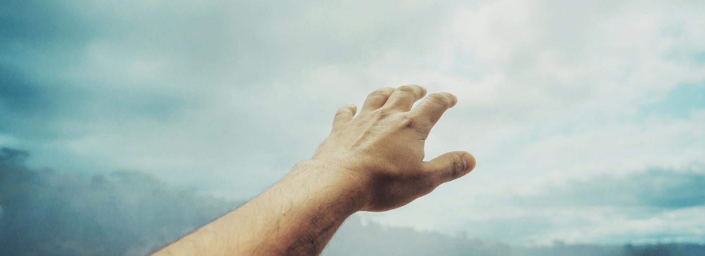 A hand reaching towards the cloudy sky at Iguazu Falls, depicting freedom and exploration.