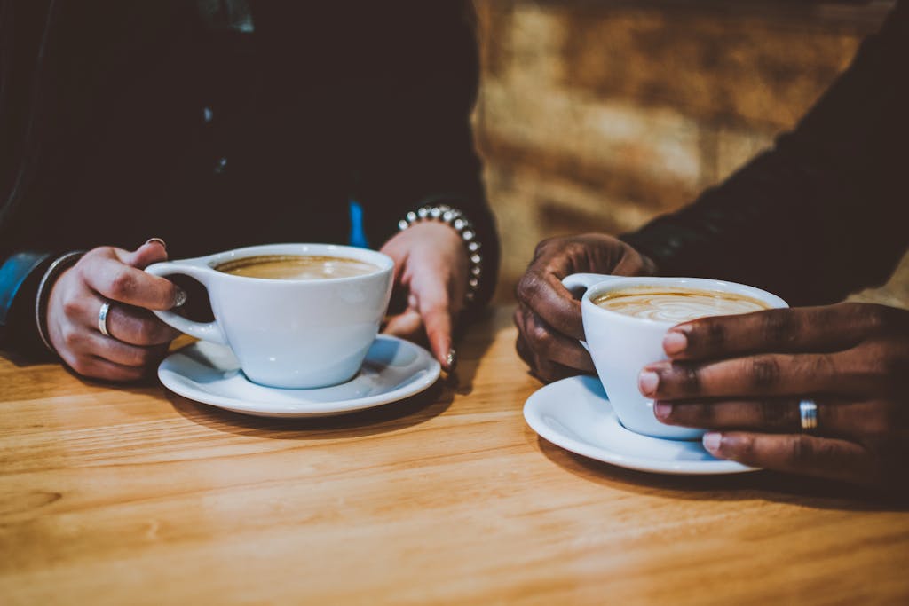 Close-up of two people holding cups of coffee at a café table, creating a cozy atmosphere.