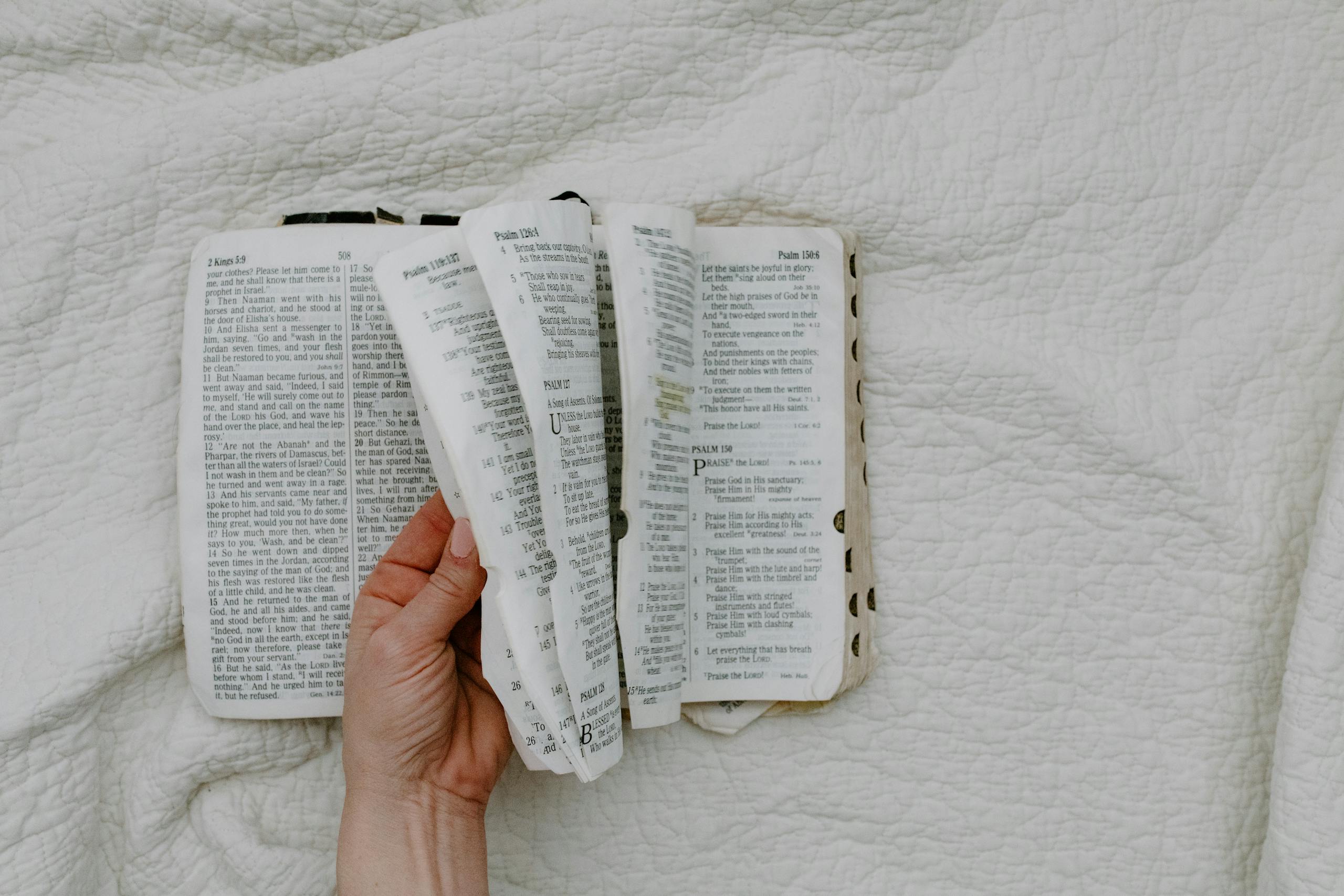 A hand gently holds an open Bible, showcasing its pages on a white fabric background.