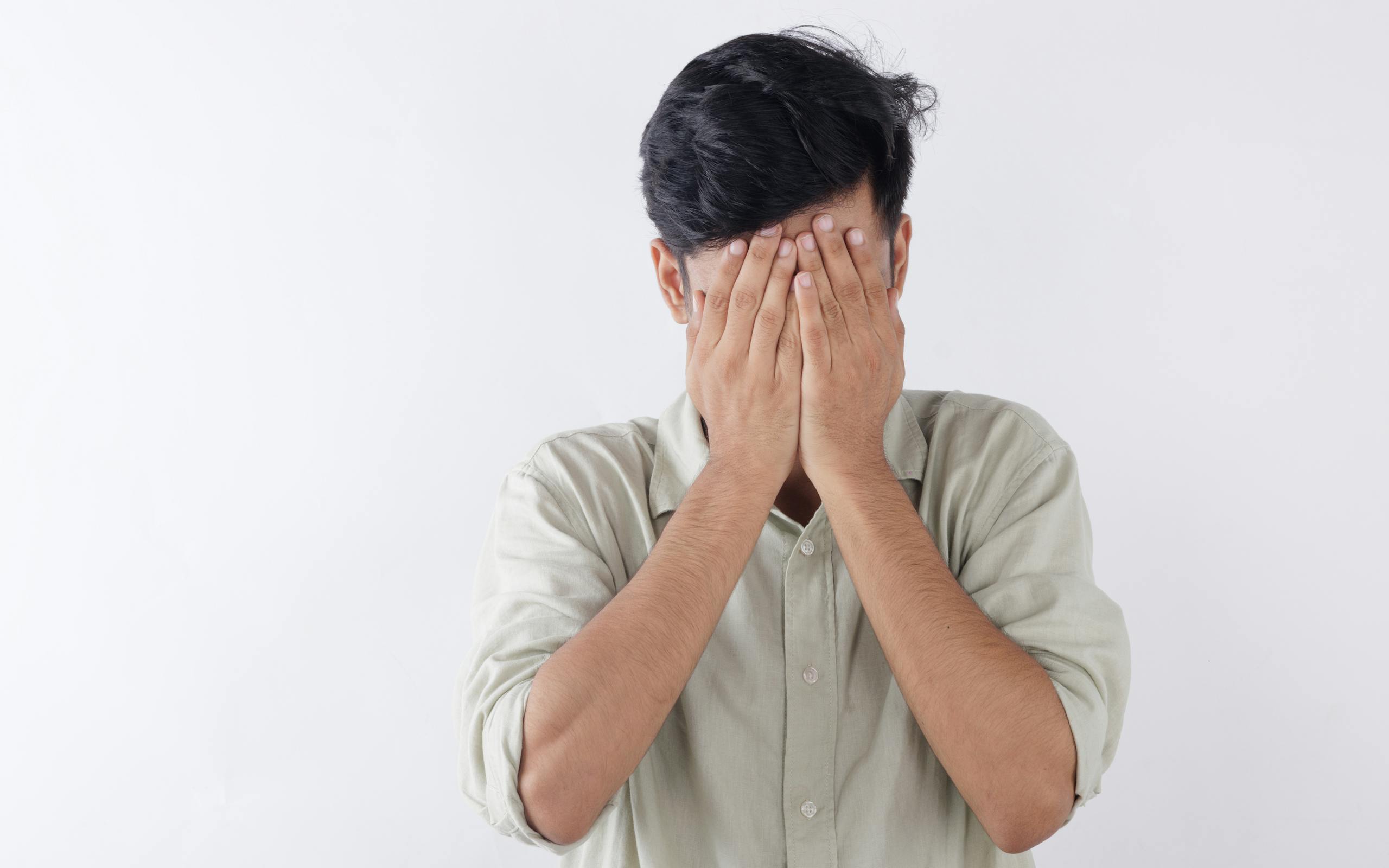 A man covering his face with hands, expressing feelings of stress and emotional struggle.